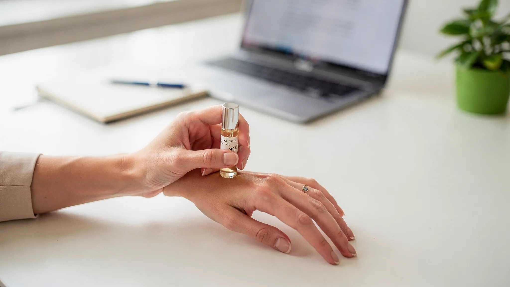 Primer plano de una mano aplicando un roll-on aromático en la muñeca, con un fondo minimalista de escritorio y una planta verde, evocando una pausa anti-estrés de un minuto en la jornada laboral.