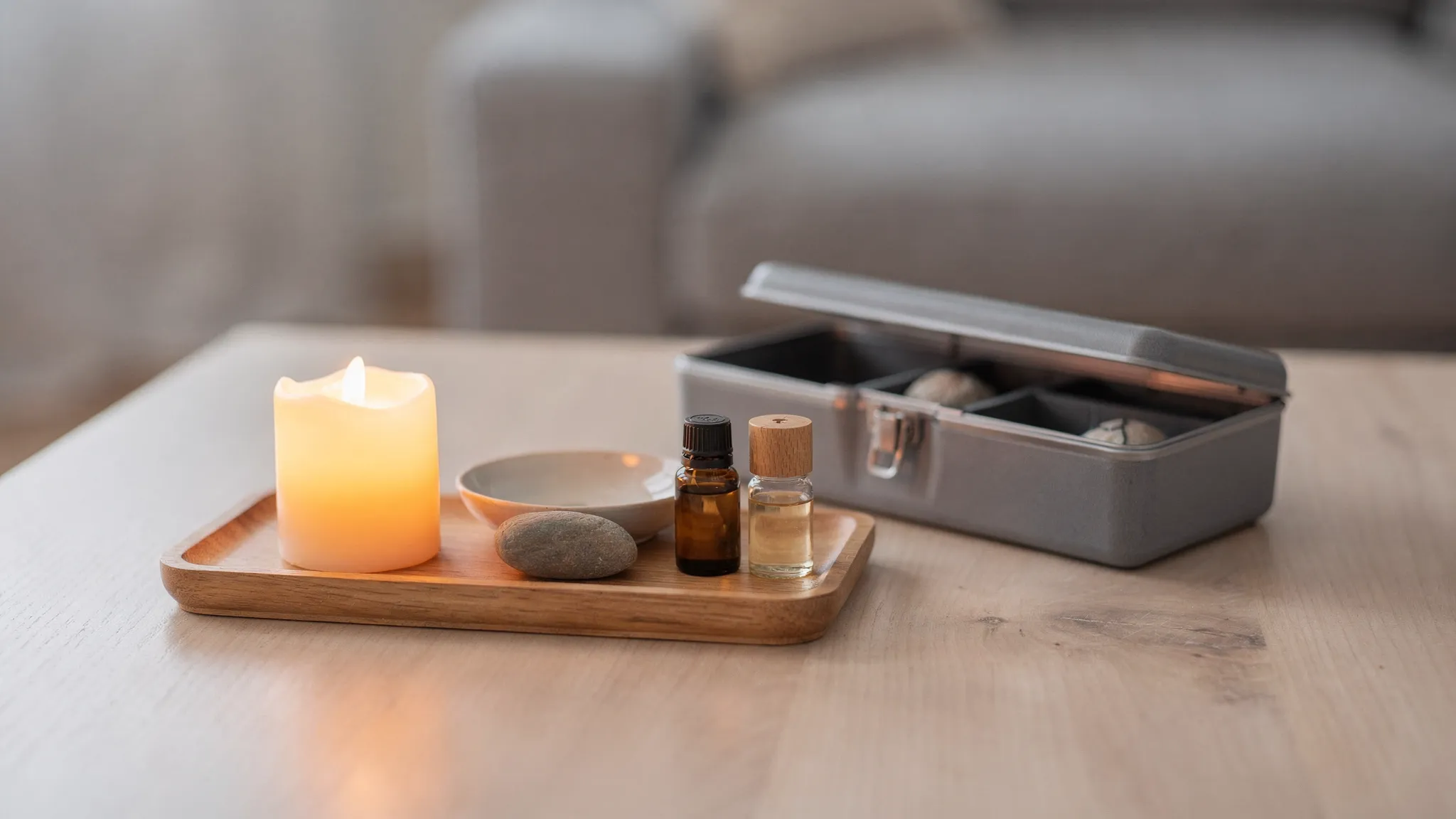 Un altar portátil de meditación: una bandeja con una vela LED, un pequeño cuenco, una botellita de aceite esencial y una piedra, junto a una caja organizadora compacta. Todo sobre una mesa limpia, pensado para guardarse fácilmente.