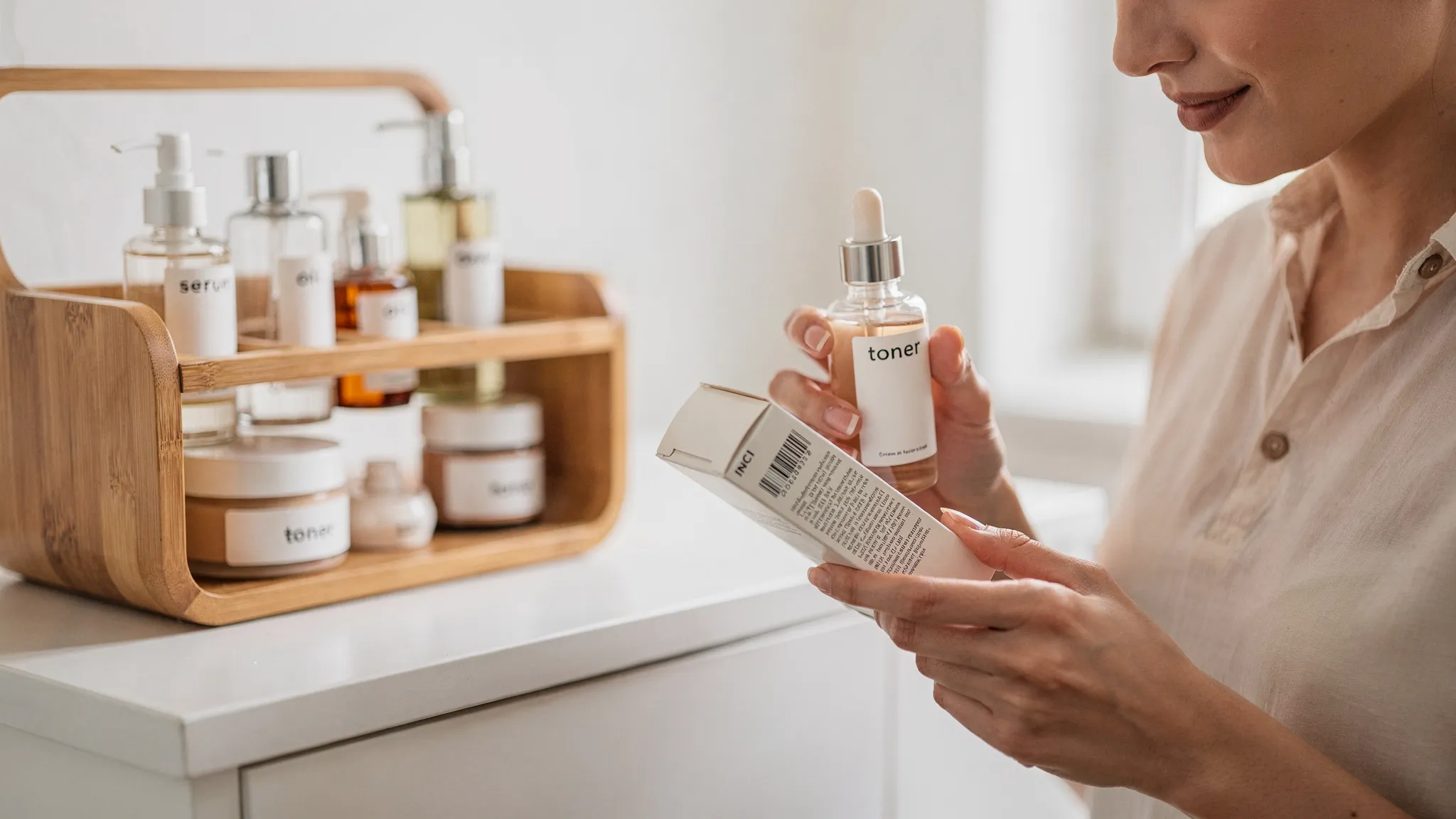 Una persona leyendo la lista INCI de una base de maquillaje junto a un organizador cosmético de bambú con frascos de vidrio y una rutina minimalista.