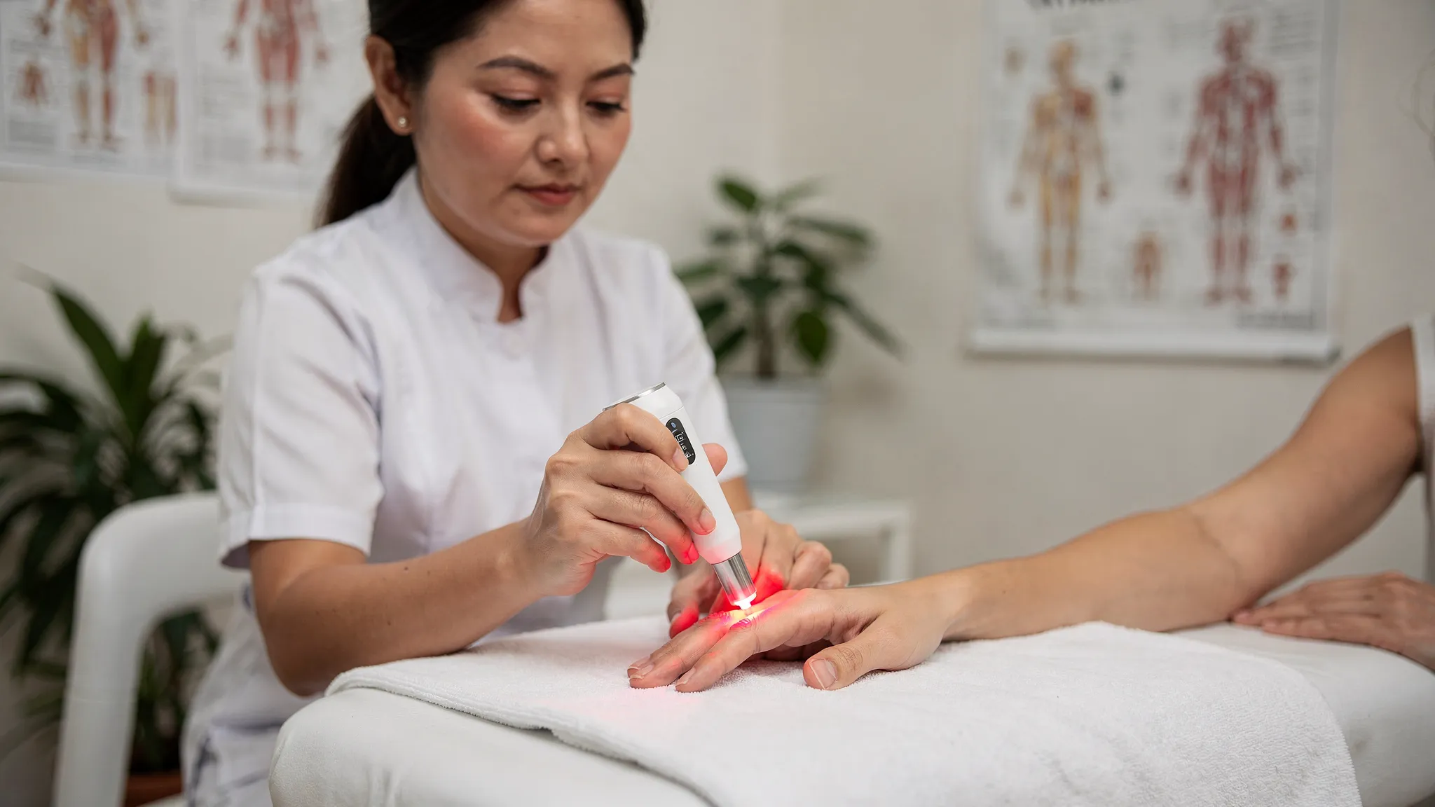 Terapeuta aplicando acupuntura con láser inalámbrico sobre un punto de la mano relacionado con garganta según mapas de acupuntura, en una consulta luminosa y calmada. El láser es pequeño, portátil y sin cables.