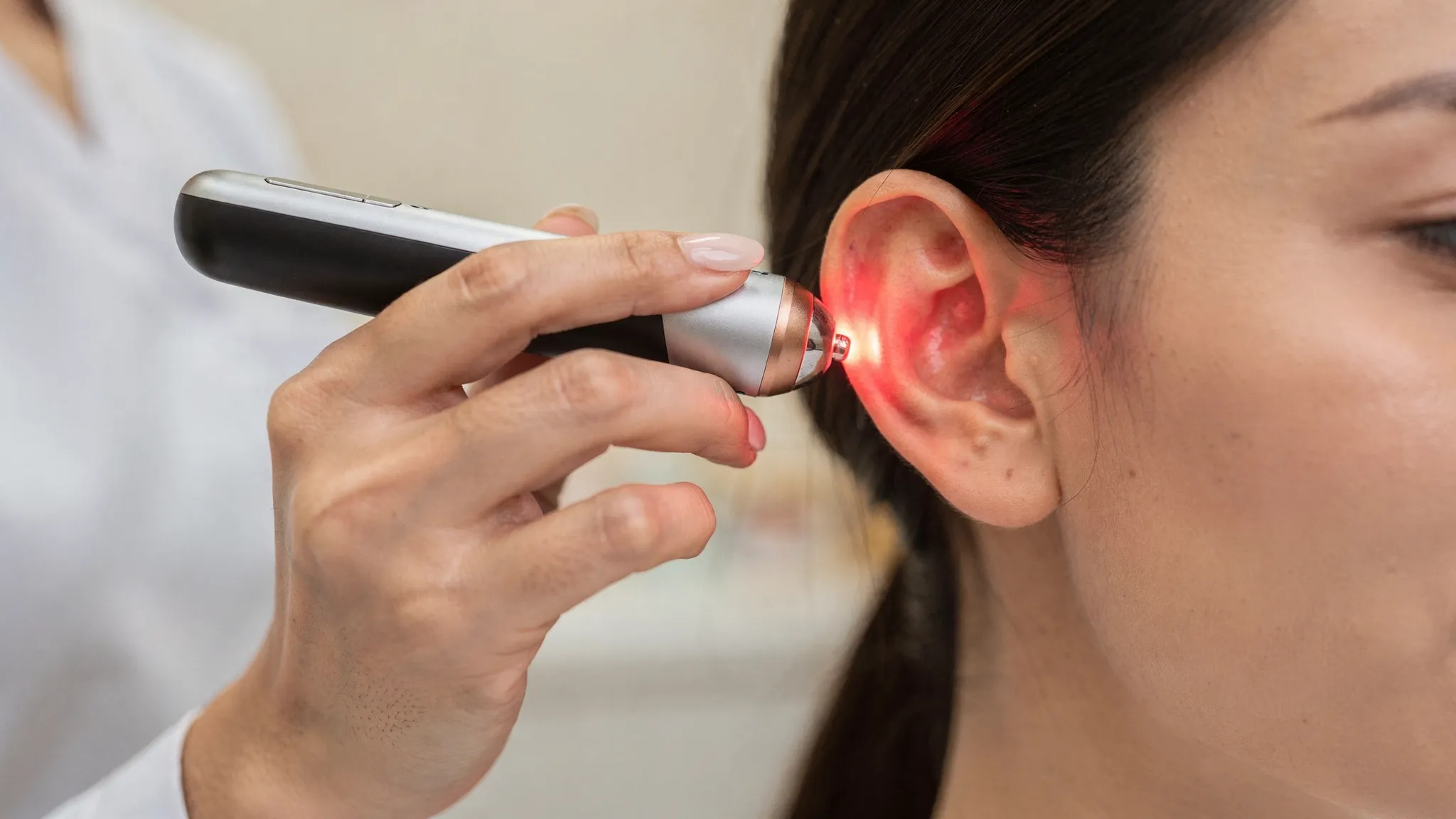 Terapeuta aplicando acupuntura láser en una oreja izquierda con un dispositivo láser inalámbrico de mano, sin cables visibles, enfocando un punto específico del pabellón auricular.