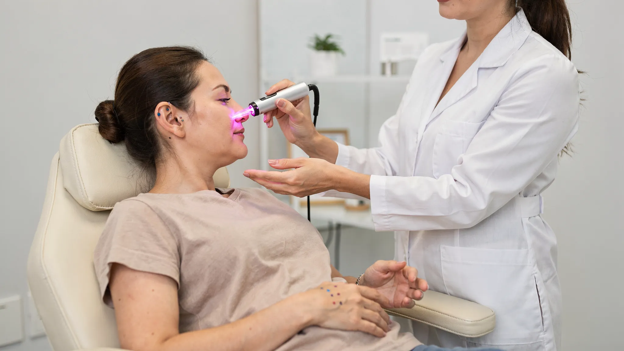 Una terapeuta aplicando acupuntura láser con un dispositivo de mano pequeño y láseres inalámbricos, sin cables, sobre puntos de la oreja y la mano en una sesión clínica tranquila.