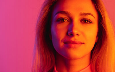 Close-up portrait of young beautiful girl tenderly looking at camera isolated over gradient studio background in neon lights